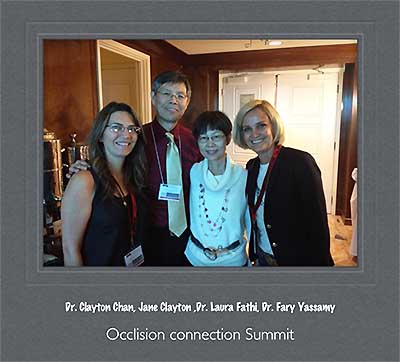 The image shows three individuals posing together, likely at an event or gathering, with a background that includes architectural details and a partial view of another person.