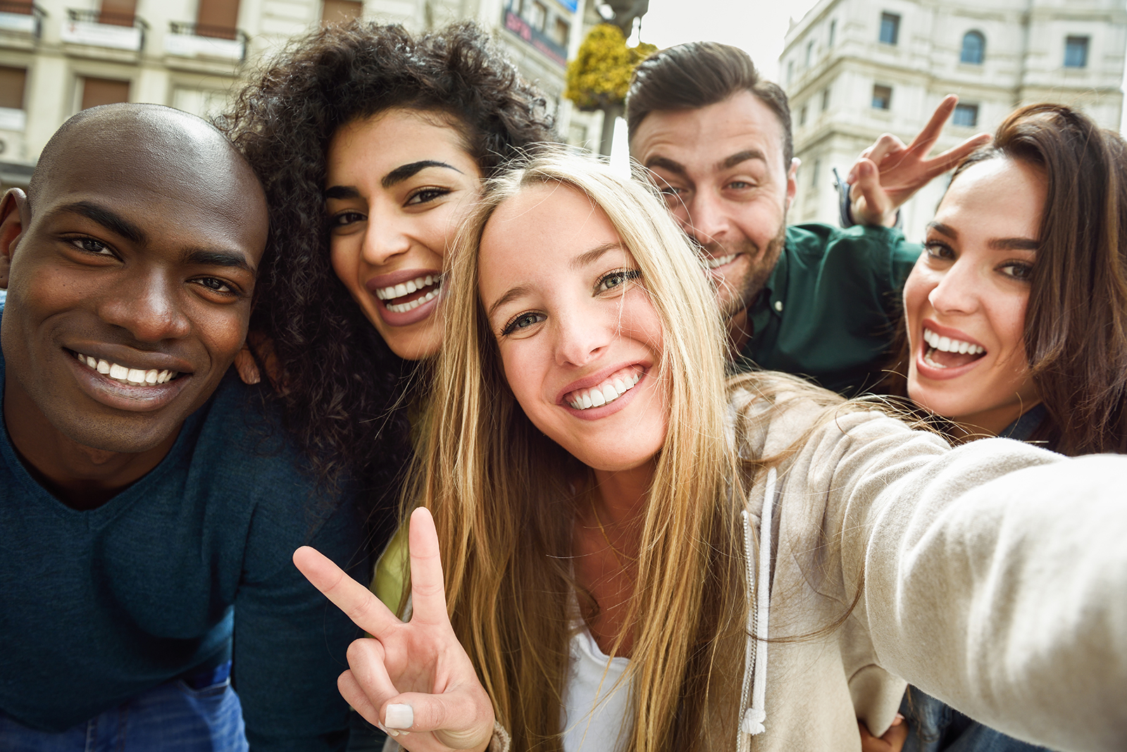 A group of young adults posing together for a selfie, smiling and appearing happy, with a city street in the background.