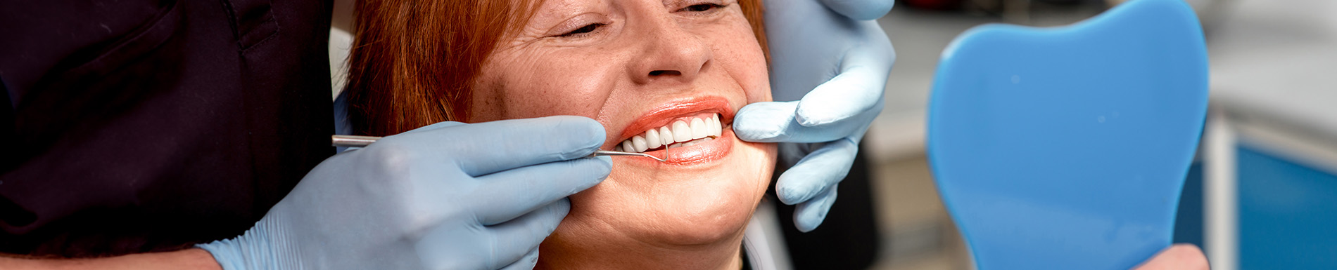 The image shows a woman sitting in a dental chair with her mouth open, receiving dental treatment, while a dental professional works on her teeth.