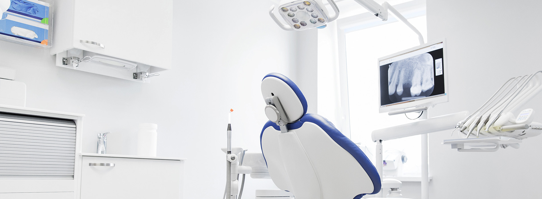 The image shows a modern dental office with a blue chair in front of a dental examination chair, indicating a space designed for dental care services.
