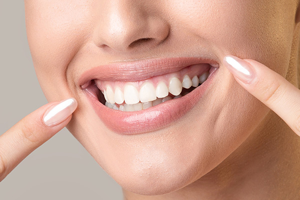 The image shows a close-up of a person's smiling face with a focus on their teeth, which are being straightened by an invisible orthodontic appliance, and they are holding up their index finger near their mouth.