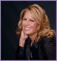 The image shows a woman posing for a portrait with a slight smile, wearing a blouse with a high collar and her hair styled in loose waves.