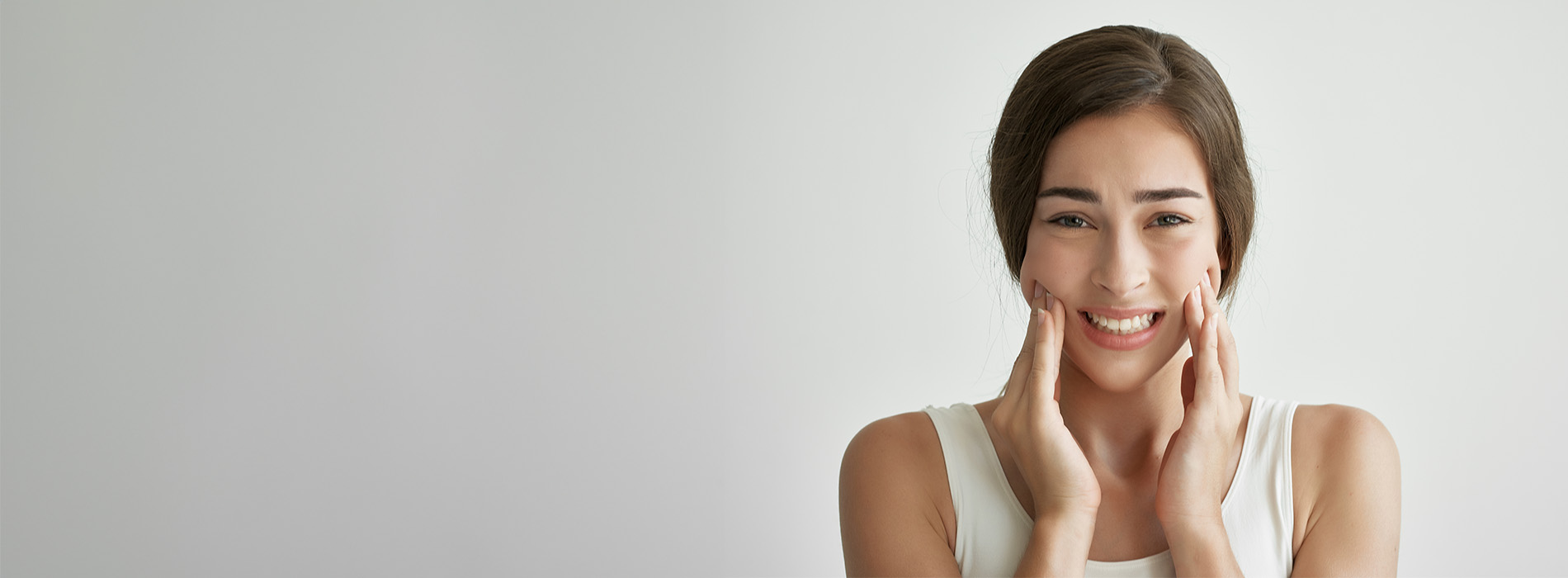The image shows a woman with her eyes closed, smiling gently, in front of a white background. She appears to be applying skincare products to her face.