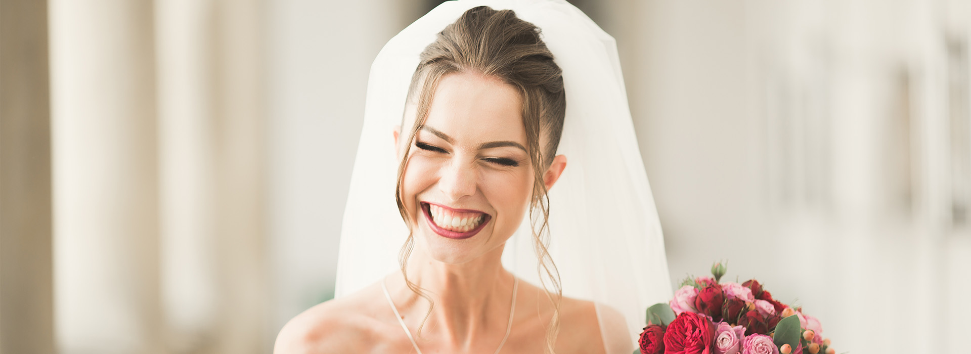 A bride wearing a white veil smiles at the camera during her wedding ceremony.