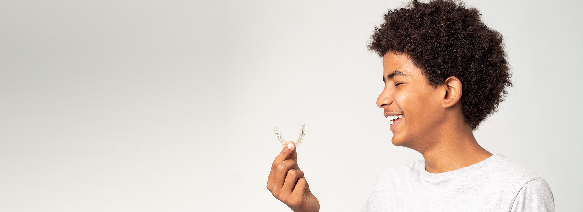 A person holds a flower with a joyful expression, against a plain background.