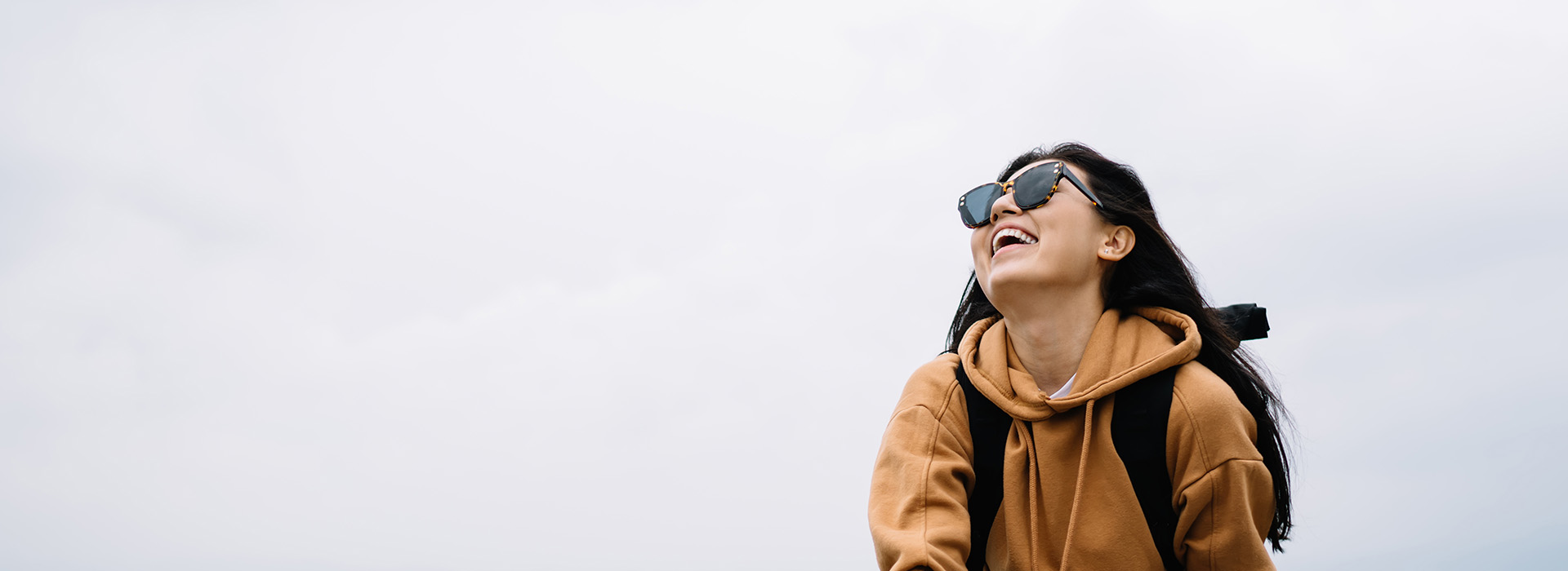 A person standing outdoors with sunglasses on their head, wearing a backpack and a hoodie, smiling at the camera.