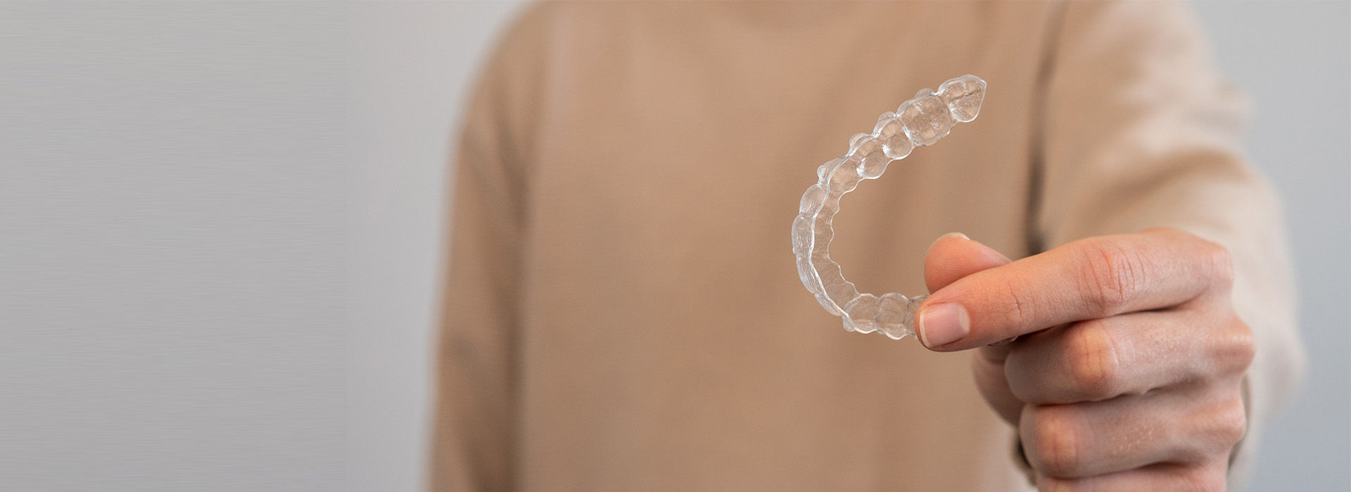 The image shows a hand holding a transparent bubble filled with water, with the background blurred but suggesting a person standing behind a white surface.