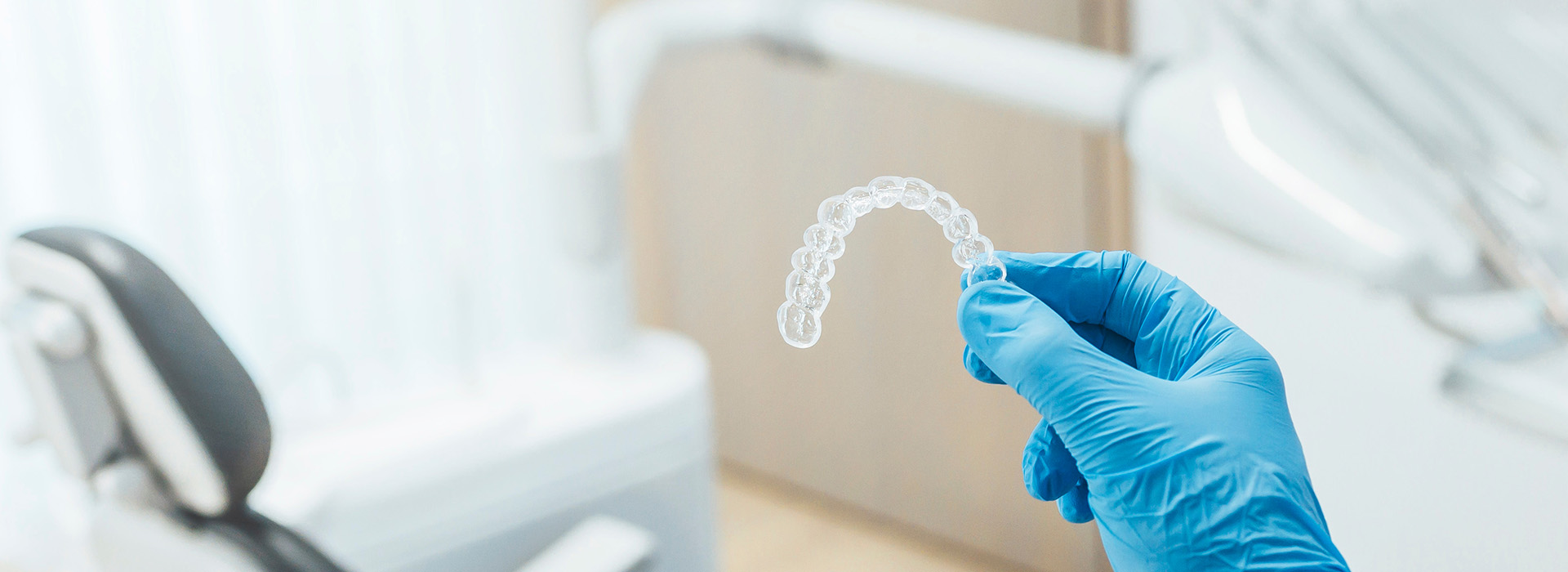 A dental office setting with a focus on a transparent dental model being held by a hand wearing blue gloves.
