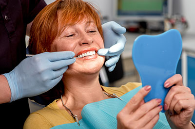 A woman in a dental chair receiving dental care with a smile on her face, holding a blue dental model.