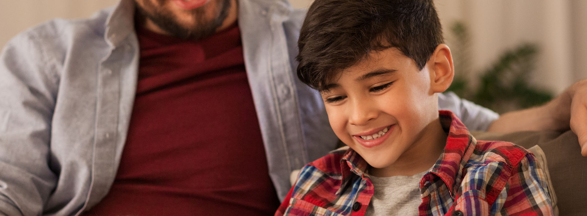 The image shows a man and a young boy sitting together on a couch, both smiling at the camera.
