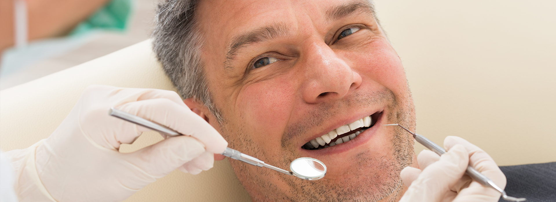 The image shows a man undergoing dental treatment, with a dentist performing work on his teeth while he is seated comfortably in a dental chair.