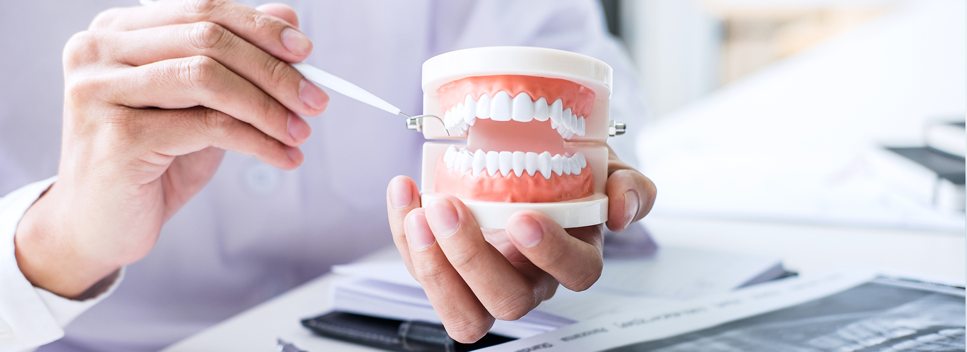 The image shows a person's hand holding a toothbrush with toothpaste, which is placed on top of a cup containing dental floss, while another hand holds a smartphone displaying a digital rendering of a mouth and teeth.