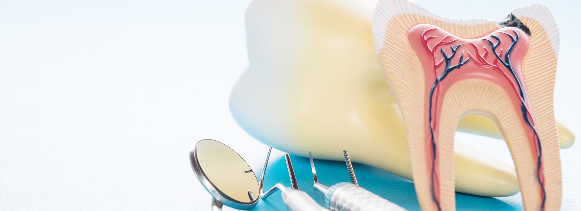 The image shows a dental model with a toothbrush and toothpaste, placed on a blue background with a sandy texture.
