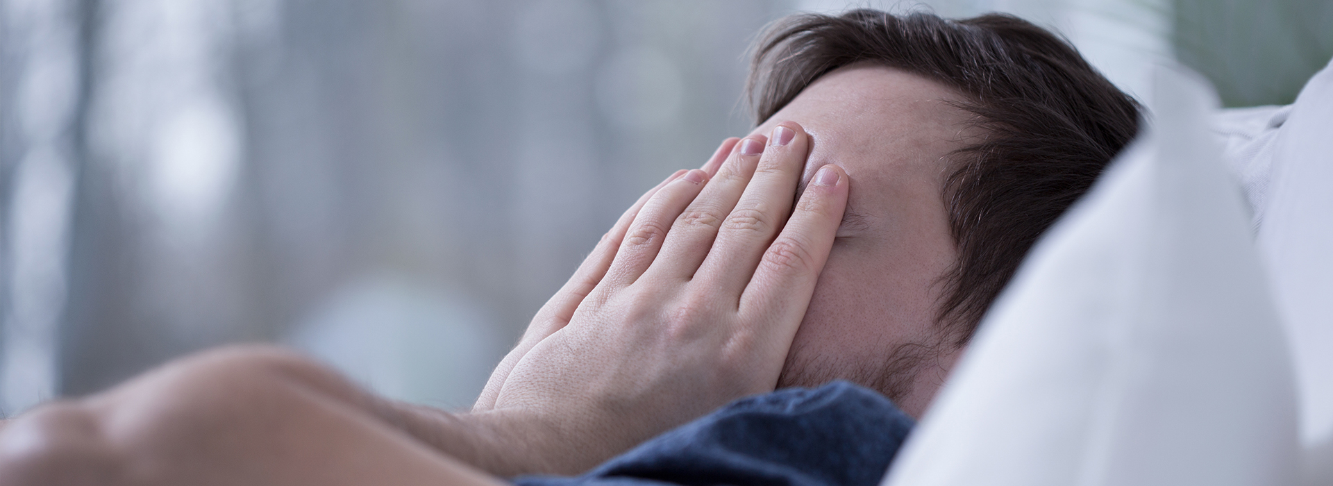 The image shows a person lying on their back with their hands covering their face, appearing to be in a state of distress or discomfort.