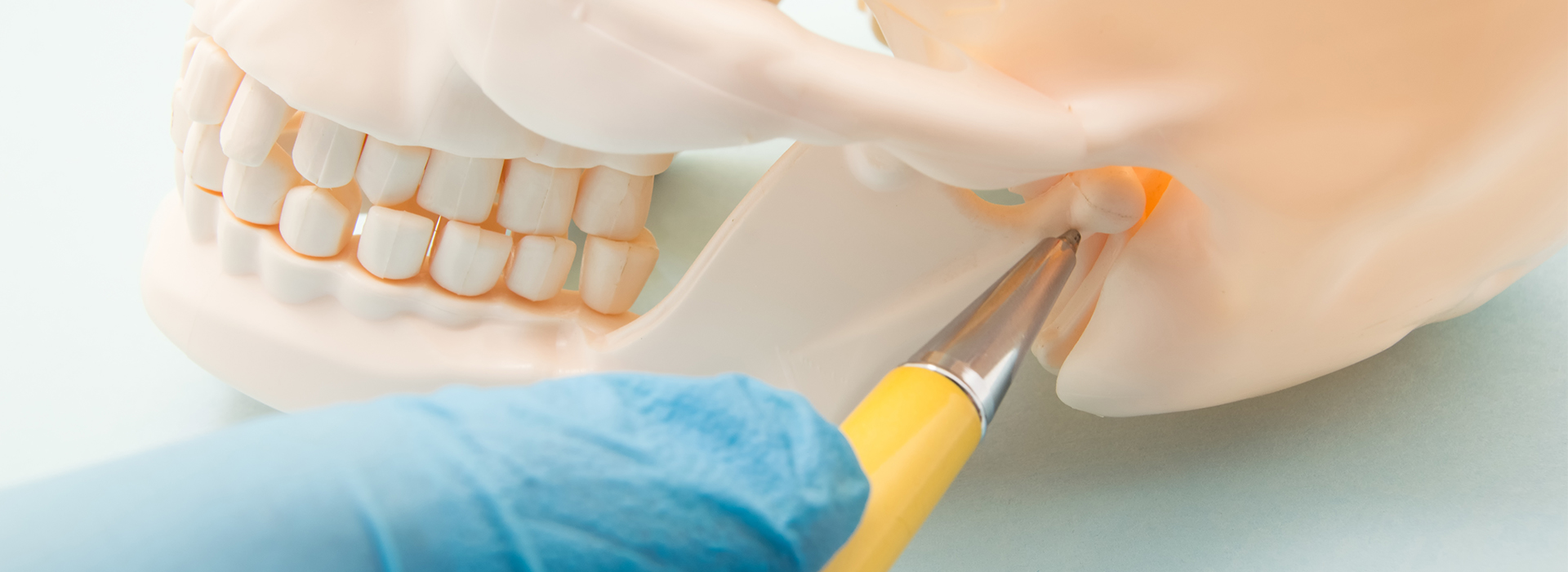 The image shows a close-up of a person's hand using a scalpel on a dental implant model, with a focus on the precision tool and the implant being worked on.