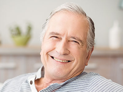 The image features an elderly man with white hair, smiling broadly, wearing a blue shirt, seated comfortably with his eyes closed, appearing relaxed and content.