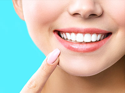 The image shows a smiling woman with white teeth, applying lipstick on her lips, against a blue background.